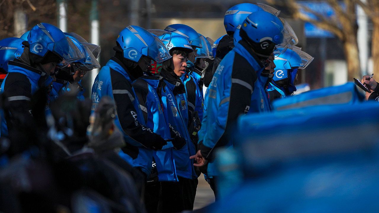 Food delivery workers on scooters gather for their daily morning briefing in Beijing