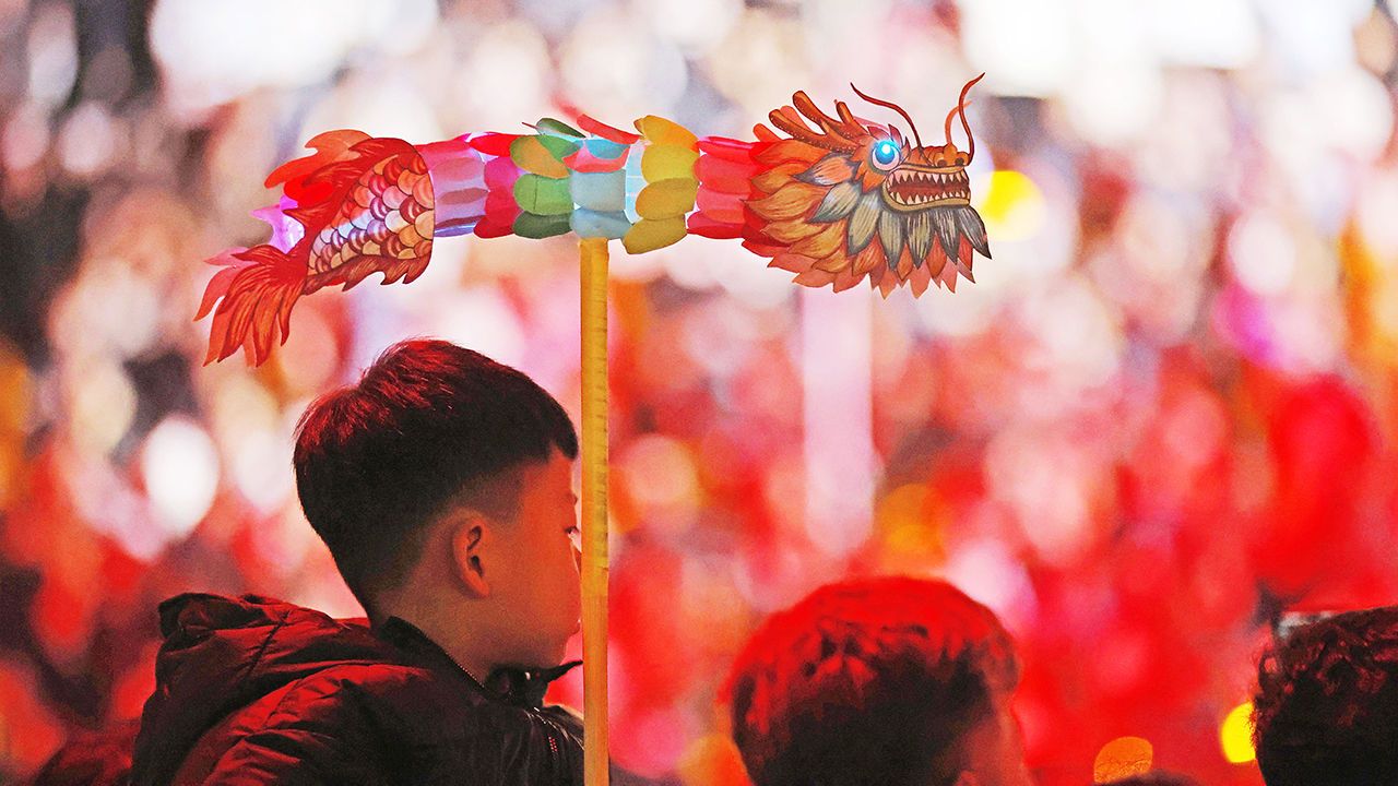 A boy holding a dragon-shaped lantern watches a show at a Spring Festival temple fair in Yancheng County, China