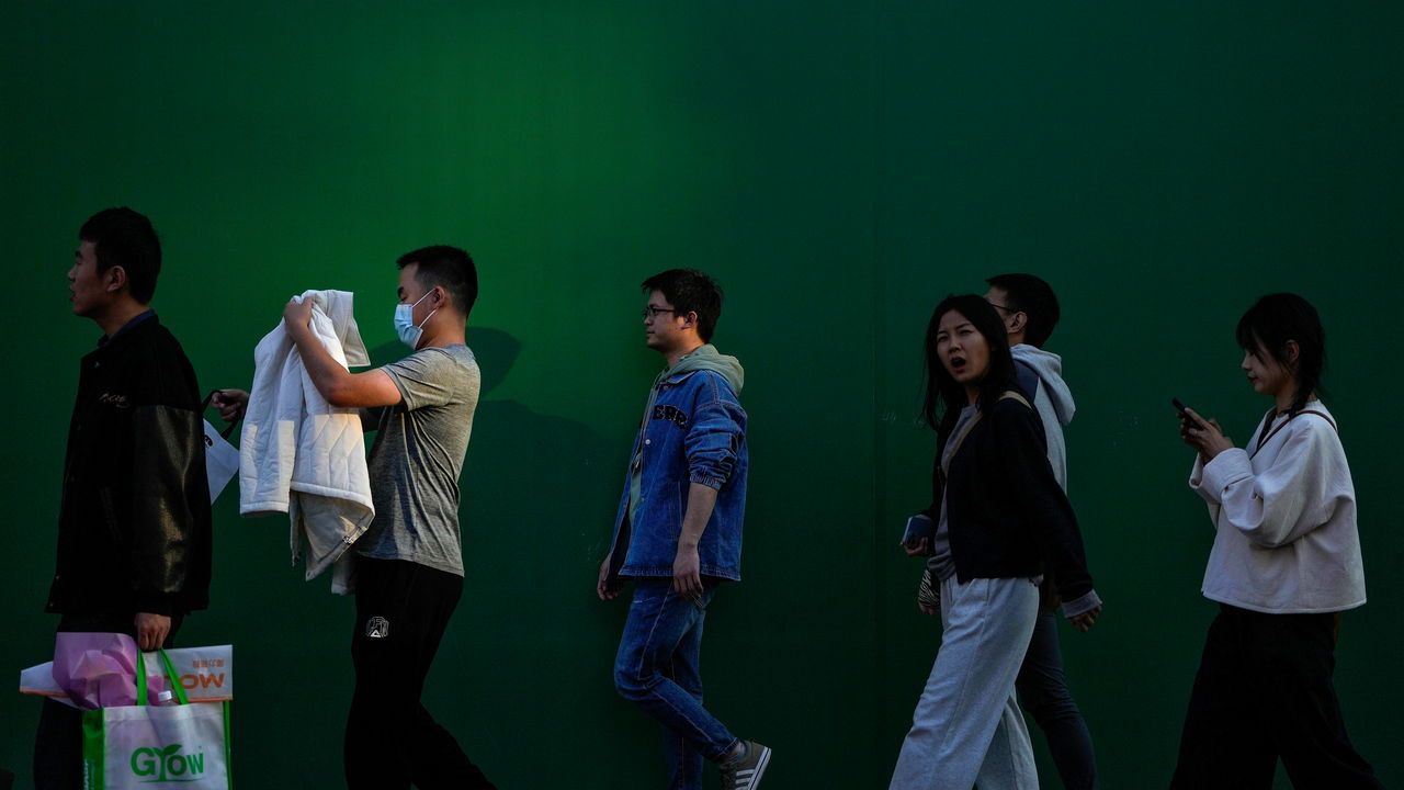 Shoppers walk by a board outside a renovation site of an outdoor shopping mall in Beijing, Sunday, Oct. 22, 2023. (AP Ph