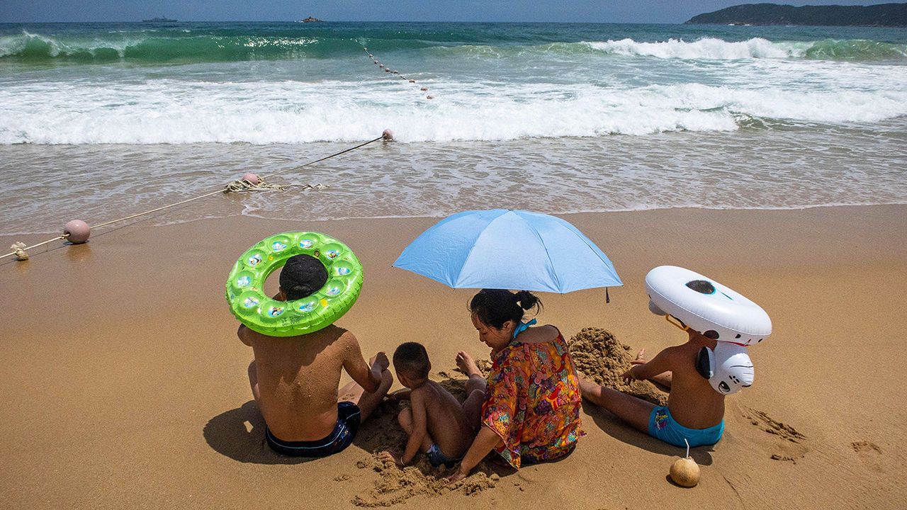 Chinese tourists sit on a beach looking out to sea.